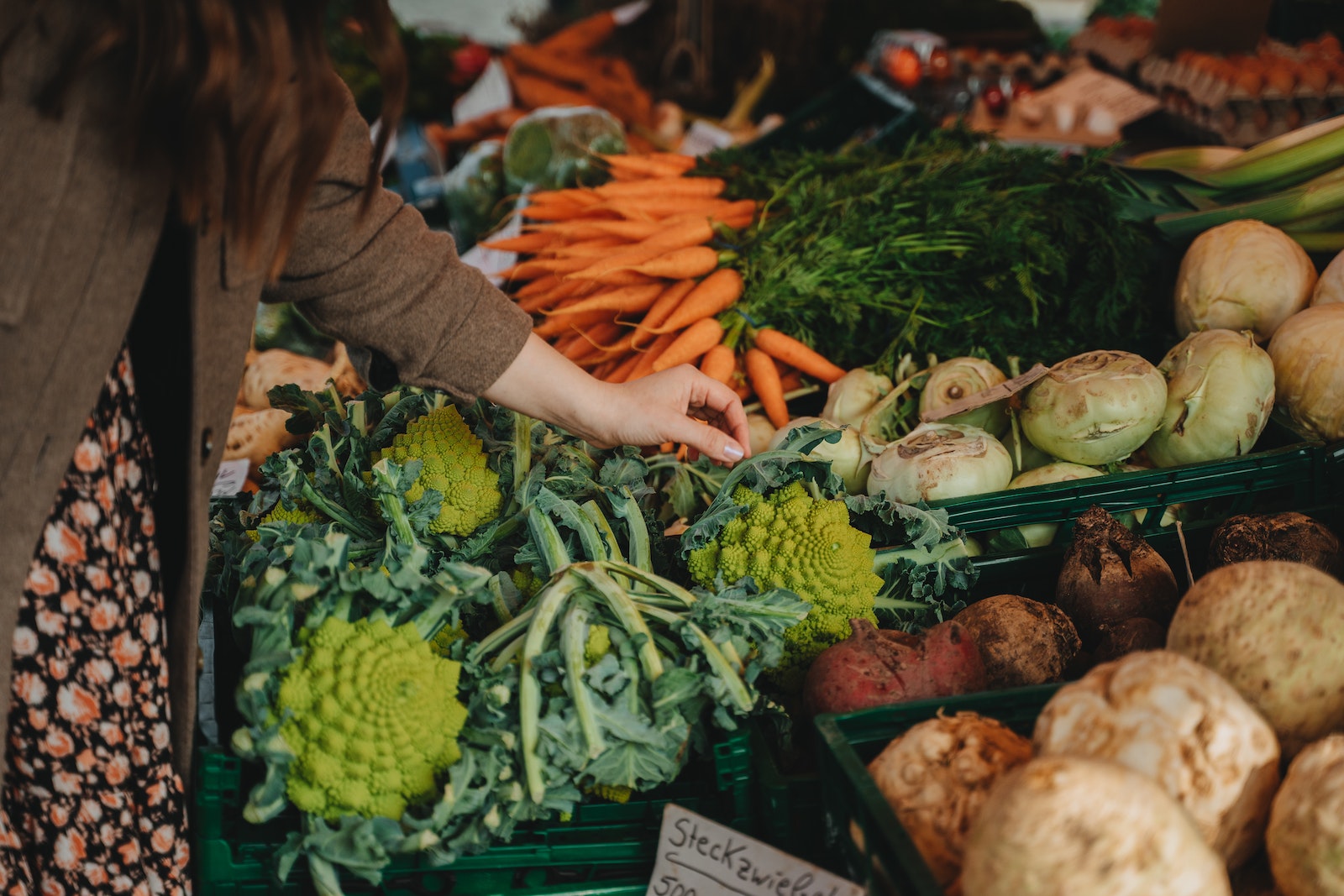  Hand of a person picking up a romanesco among other vegetables in a well-stocked stand