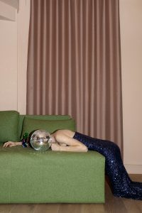 Woman in fancy dress laying exhausted and overwhelmed on a surface. Her head is a disco ball